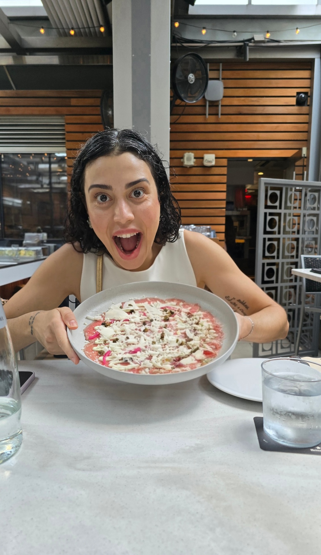 Marianna sorrindo à mesa com um prato de carpaccio